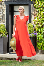 Woman in a red dress standing outdoors with plants and a door in the background