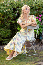 Buy Online Claudia Dress Alice Collins Woman in a floral dress sitting on a chair in a garden