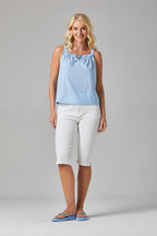 Buy Online Kata Top Alice Collins - Woman wearing a light blue sleeveless top and white pants on a gray background