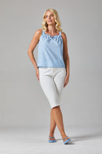 Buy Online Kata Top Alice Collins - Woman wearing a light blue sleeveless top and white pants on a gray background