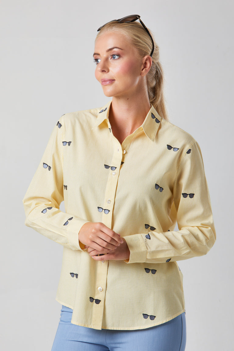 Woman wearing a light yellow shirt with small black and blue patterns on a plain background
