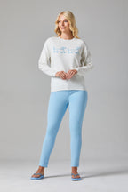 Buy Online Jessie & Pippa Pullover Alice Collins - Woman wearing a white sweater with a graphic design and light blue pants on a gray background