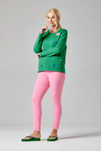 Buy Online Nicola Pullover Alice Collins - Woman wearing a green sweater with blue dots and pink pants on a gray background