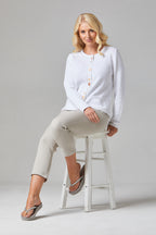 Buy Multi Button Cardigan Online - Alice Collins - Woman sitting on a white stool wearing a white cardigan and beige pants against a gray background