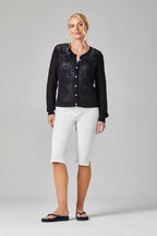 Woman wearing a black lace cardigan and white pants on a gray background